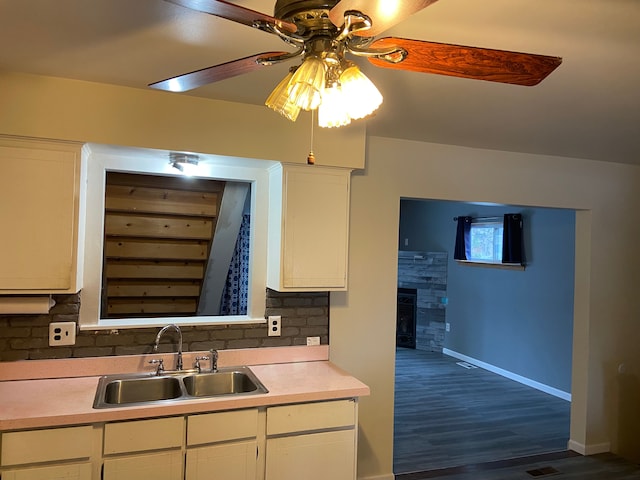 kitchen with white cabinets, a stone fireplace, sink, ceiling fan, and tasteful backsplash