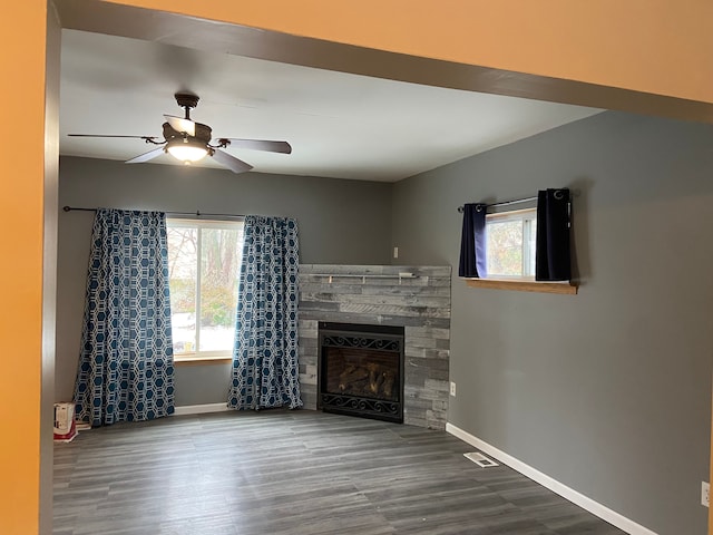 unfurnished living room with hardwood / wood-style floors, a stone fireplace, and ceiling fan