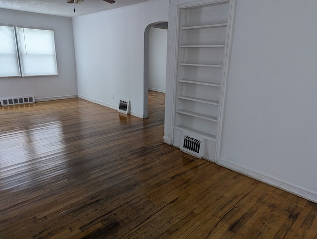 empty room with a textured ceiling, ceiling fan, built in features, and dark wood-type flooring