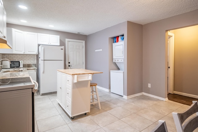 kitchen featuring a center island, a textured ceiling, stacked washer / drying machine, white fridge, and white cabinetry