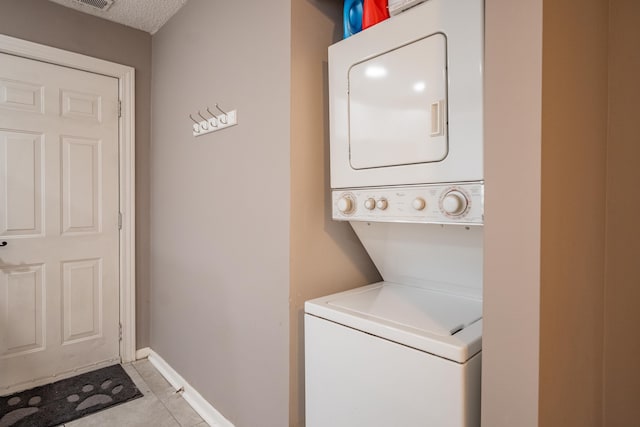 laundry room featuring light tile patterned floors, stacked washing maching and dryer, and a textured ceiling