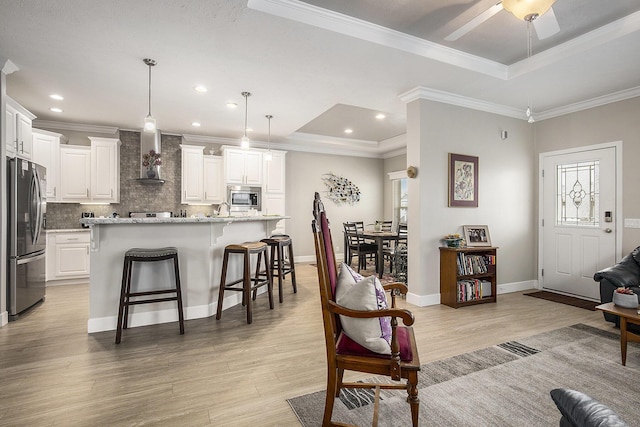 kitchen featuring hanging light fixtures, stainless steel appliances, a raised ceiling, a kitchen island with sink, and white cabinets