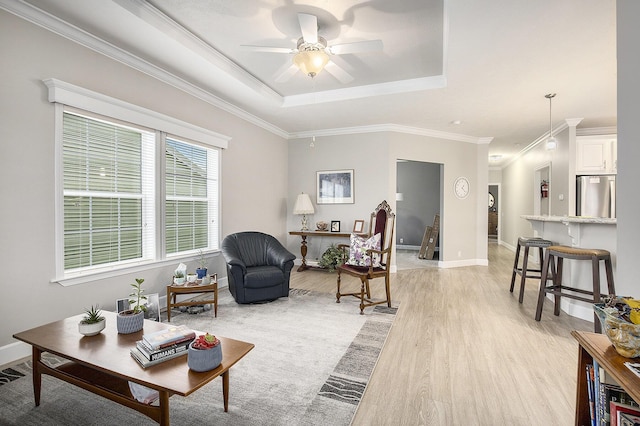 living room with ceiling fan, light hardwood / wood-style floors, a raised ceiling, and ornamental molding