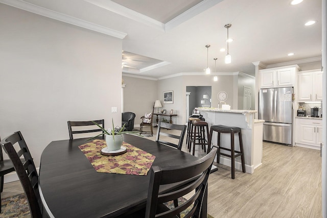 dining room with a raised ceiling, light wood-type flooring, and ornamental molding