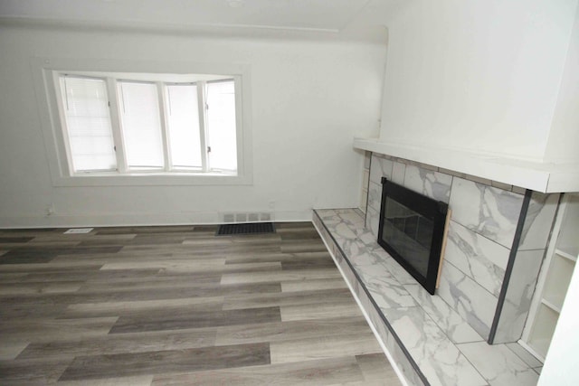 unfurnished living room with wood-type flooring and a tiled fireplace