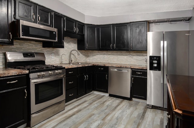 kitchen with light stone countertops, sink, stainless steel appliances, tasteful backsplash, and light hardwood / wood-style floors