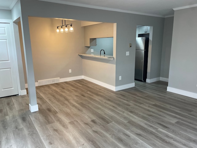interior space with sink, ornamental molding, kitchen peninsula, stainless steel fridge, and hardwood / wood-style flooring