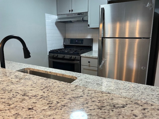 kitchen featuring backsplash, light stone countertops, sink, and stainless steel appliances