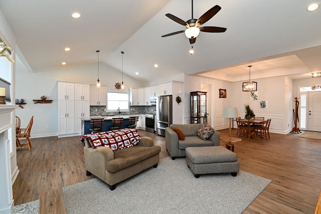 living room with lofted ceiling, plenty of natural light, ceiling fan with notable chandelier, and light wood-type flooring