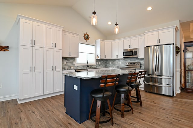 kitchen with light stone countertops, stainless steel appliances, white cabinetry, and a kitchen island