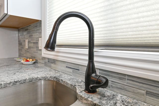 interior details featuring light stone counters, sink, and backsplash