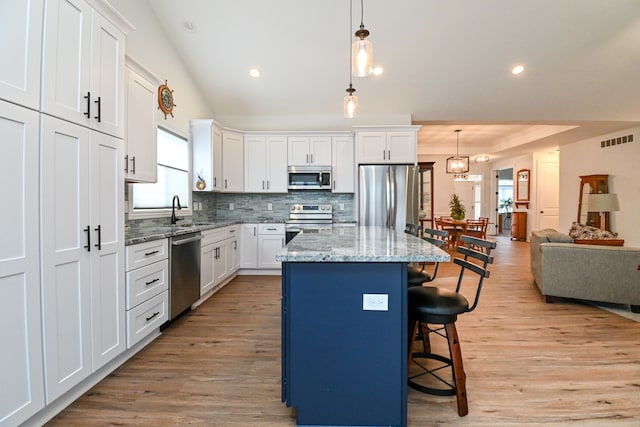 kitchen with appliances with stainless steel finishes, a breakfast bar, pendant lighting, white cabinets, and a kitchen island