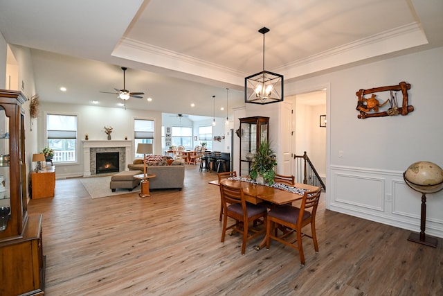 dining room featuring ceiling fan with notable chandelier, wood-type flooring, ornamental molding, and a tray ceiling