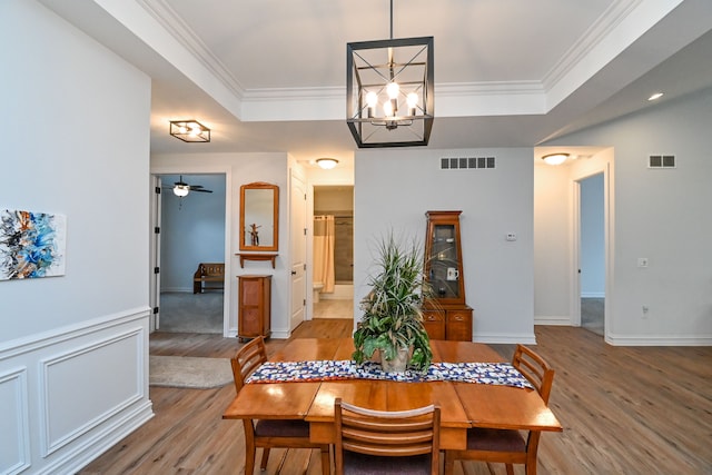 dining area with a raised ceiling, crown molding, ceiling fan with notable chandelier, and light wood-type flooring