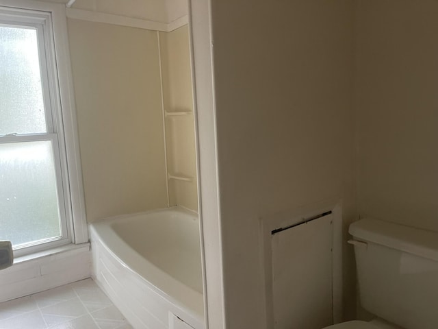 bathroom featuring tile patterned flooring, a tub to relax in, toilet, and plenty of natural light