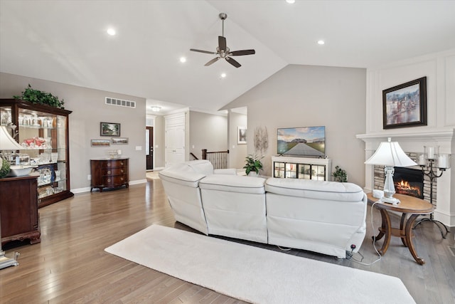 living room featuring ceiling fan, vaulted ceiling, a stone fireplace, and light hardwood / wood-style flooring