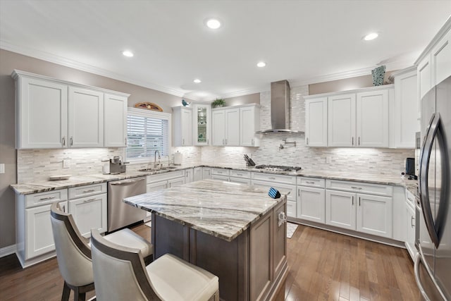 kitchen featuring white cabinetry, sink, wall chimney range hood, a kitchen island, and appliances with stainless steel finishes