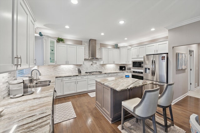 kitchen with light stone counters, wall chimney exhaust hood, stainless steel appliances, sink, and white cabinetry