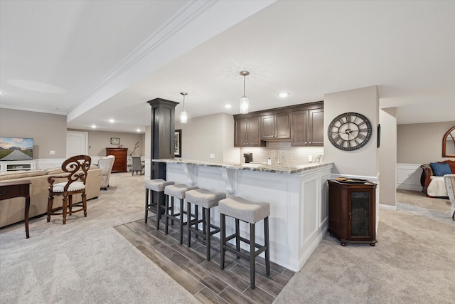 kitchen featuring decorative columns, ornamental molding, a breakfast bar, dark brown cabinets, and decorative light fixtures