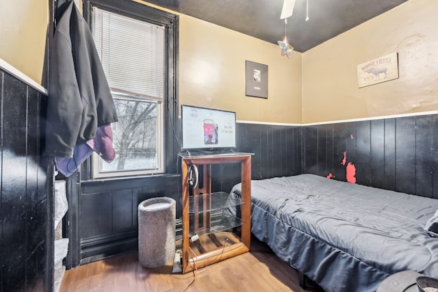 bedroom with hardwood / wood-style floors, ceiling fan, and wooden walls