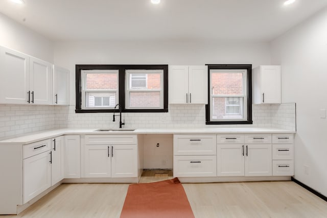 kitchen with backsplash, white cabinetry, sink, and light hardwood / wood-style flooring