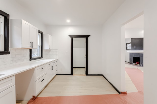 kitchen with backsplash, white cabinets, light hardwood / wood-style floors, and a brick fireplace