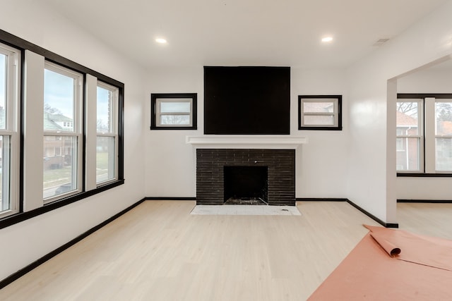 unfurnished living room with a healthy amount of sunlight, light hardwood / wood-style flooring, and a brick fireplace