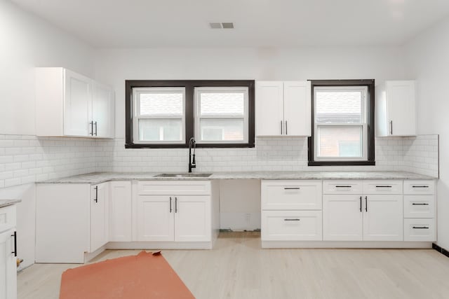 kitchen featuring tasteful backsplash, white cabinetry, sink, and light stone countertops