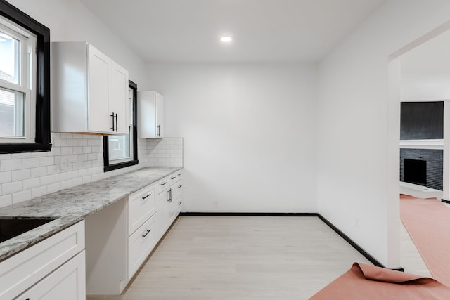 kitchen with light stone countertops, tasteful backsplash, white cabinetry, and light hardwood / wood-style flooring