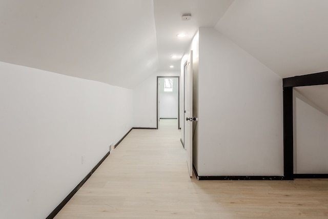 corridor featuring light wood-type flooring and vaulted ceiling