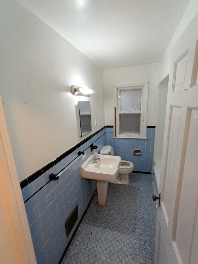 bathroom featuring a bath, toilet, and tile walls