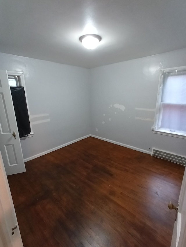 unfurnished room featuring baseboard heating and dark wood-type flooring