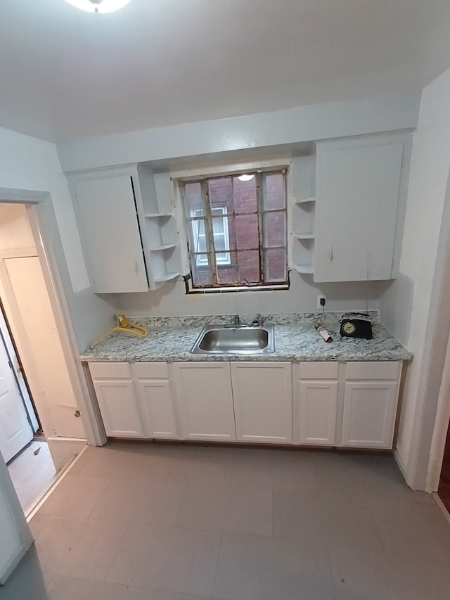 kitchen with white cabinets, light stone countertops, and sink