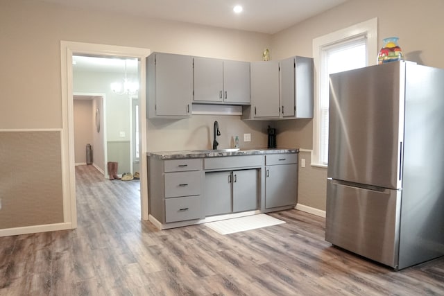 kitchen with stainless steel fridge, gray cabinetry, sink, an inviting chandelier, and light hardwood / wood-style floors