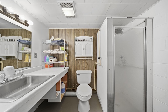 bathroom with wood walls, toilet, a shower with shower door, and sink