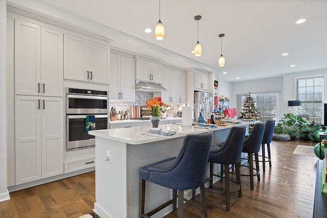 kitchen with a kitchen island with sink, hanging light fixtures, white cabinetry, and stainless steel appliances