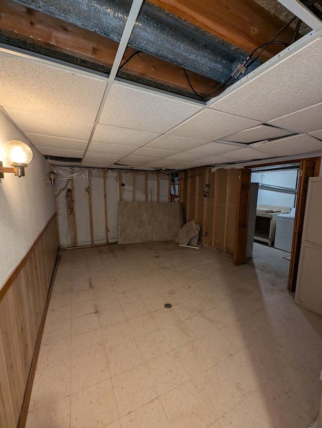 basement featuring a drop ceiling, wooden walls, and separate washer and dryer