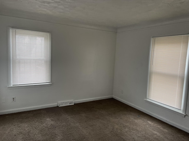 unfurnished room featuring dark carpet and a textured ceiling