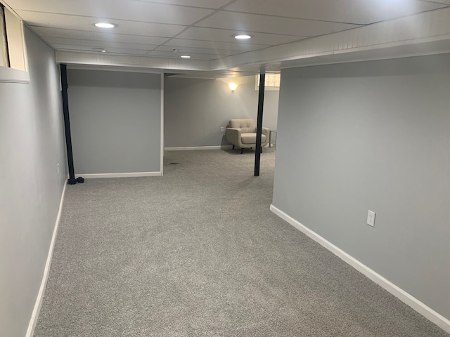 basement with a paneled ceiling and light colored carpet