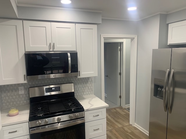 kitchen with white cabinets, ornamental molding, and stainless steel appliances