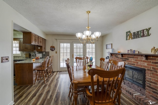 dining space featuring an inviting chandelier, dark hardwood / wood-style flooring, a textured ceiling, and a brick fireplace