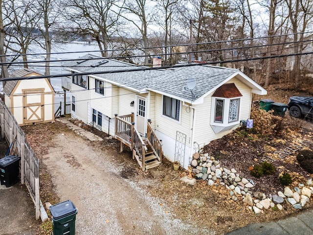 view of front of property featuring roof with shingles, dirt driveway, a storage shed, fence, and an outdoor structure