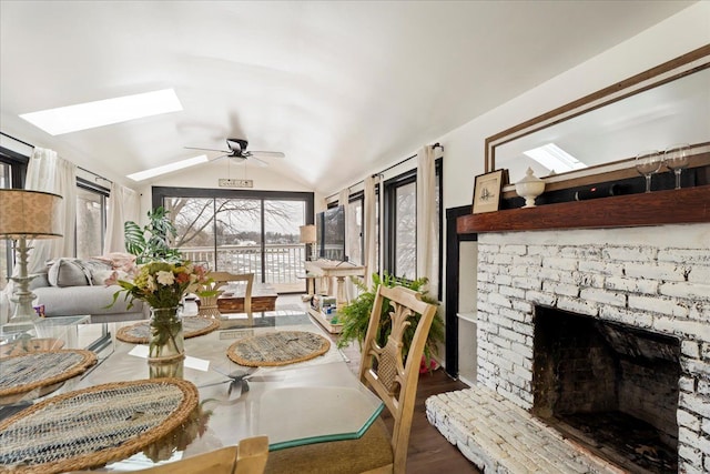 dining area with lofted ceiling with skylight, wood finished floors, a fireplace, and ceiling fan