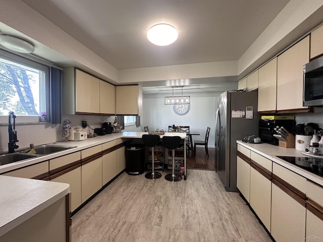 kitchen featuring sink, appliances with stainless steel finishes, light hardwood / wood-style floors, decorative light fixtures, and cream cabinetry