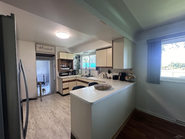 kitchen with light hardwood / wood-style floors, stainless steel fridge, kitchen peninsula, and sink