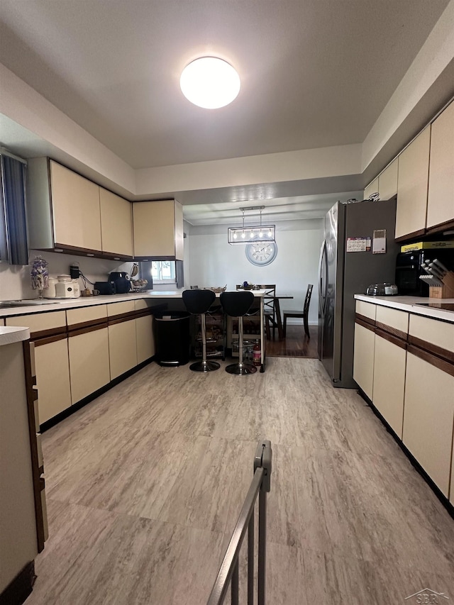 kitchen with cream cabinets, decorative light fixtures, light hardwood / wood-style floors, and stainless steel refrigerator