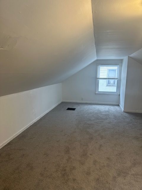 bonus room with dark carpet and vaulted ceiling