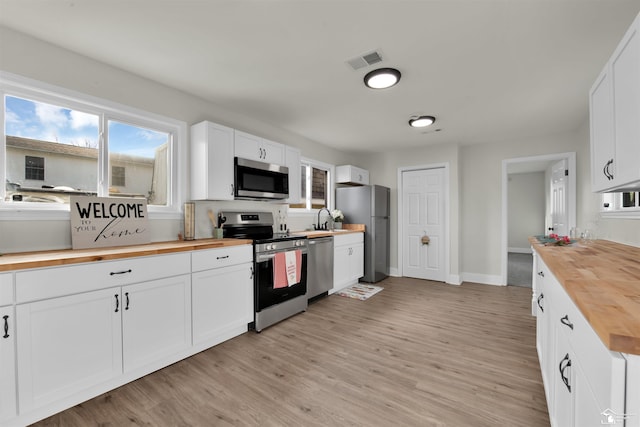 kitchen with white cabinets, appliances with stainless steel finishes, butcher block countertops, and sink