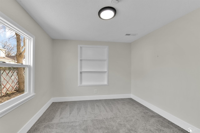 unfurnished room with built in shelves, light carpet, plenty of natural light, and a textured ceiling