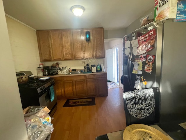 kitchen featuring black range oven, stainless steel fridge, light wood-type flooring, and sink